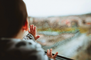 child peering out window lookng at rain