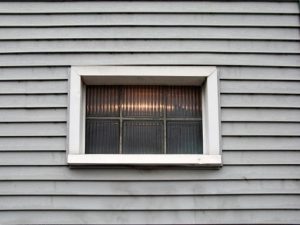 older house with siding that needs replacement and one glass block window