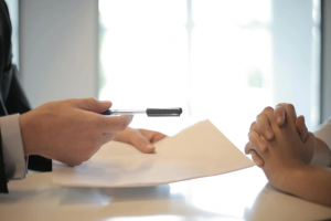 person handing paperwork and pen to another person