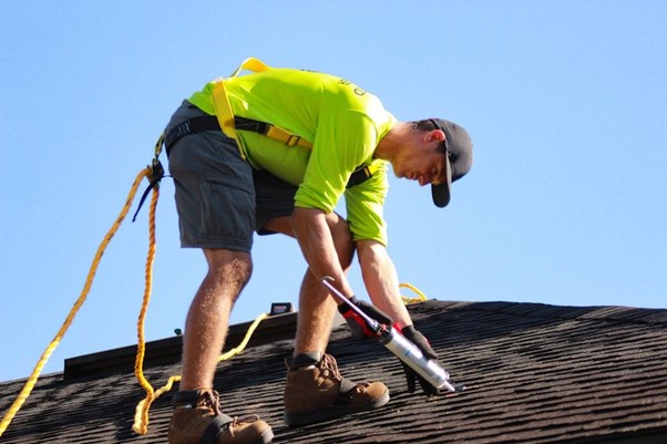 Man on roof caulking shingles and wearing safety equipment