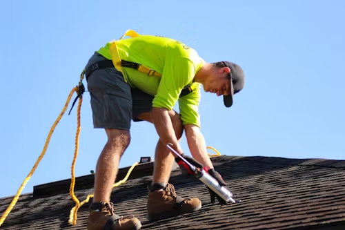 roofer wearing safety equipment caulking roof shingles