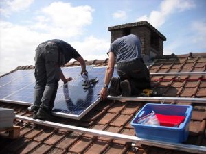 two men on roof installing solar panels with box of tools