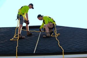 two men wearing safety equipment working on roof