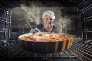 woman taking steaming hot pie from oven