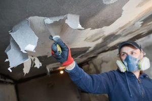 worker scraping ruined wall paper