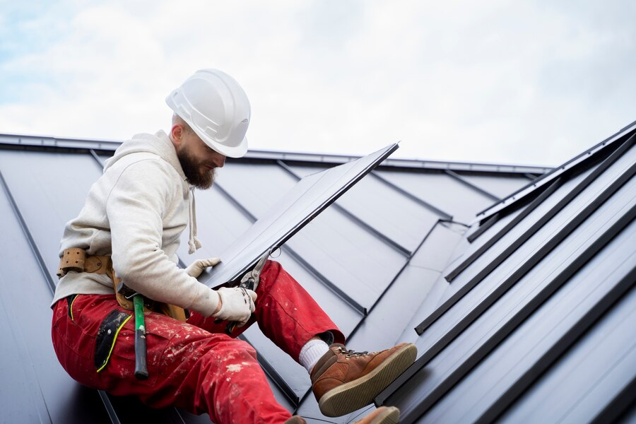 roofer sitting on metal roof holding panel