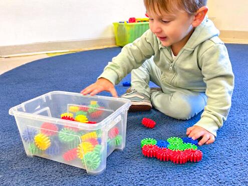 A child enjoys playing with toys in a plastic container, surrounded by a warm and inviting carpet.