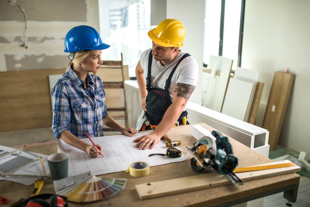Female foreman and manual worker talking while analyzing blueprints at construction site.