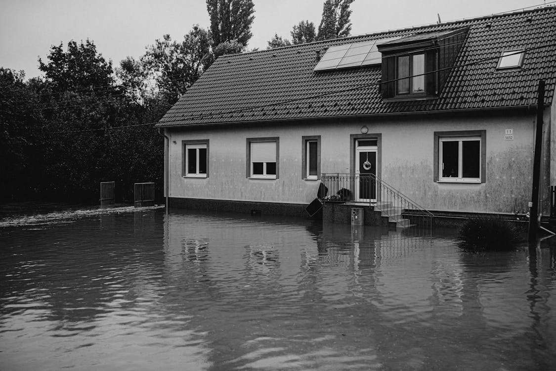 flood-house a black and white photo of a house with floodwater in front of it