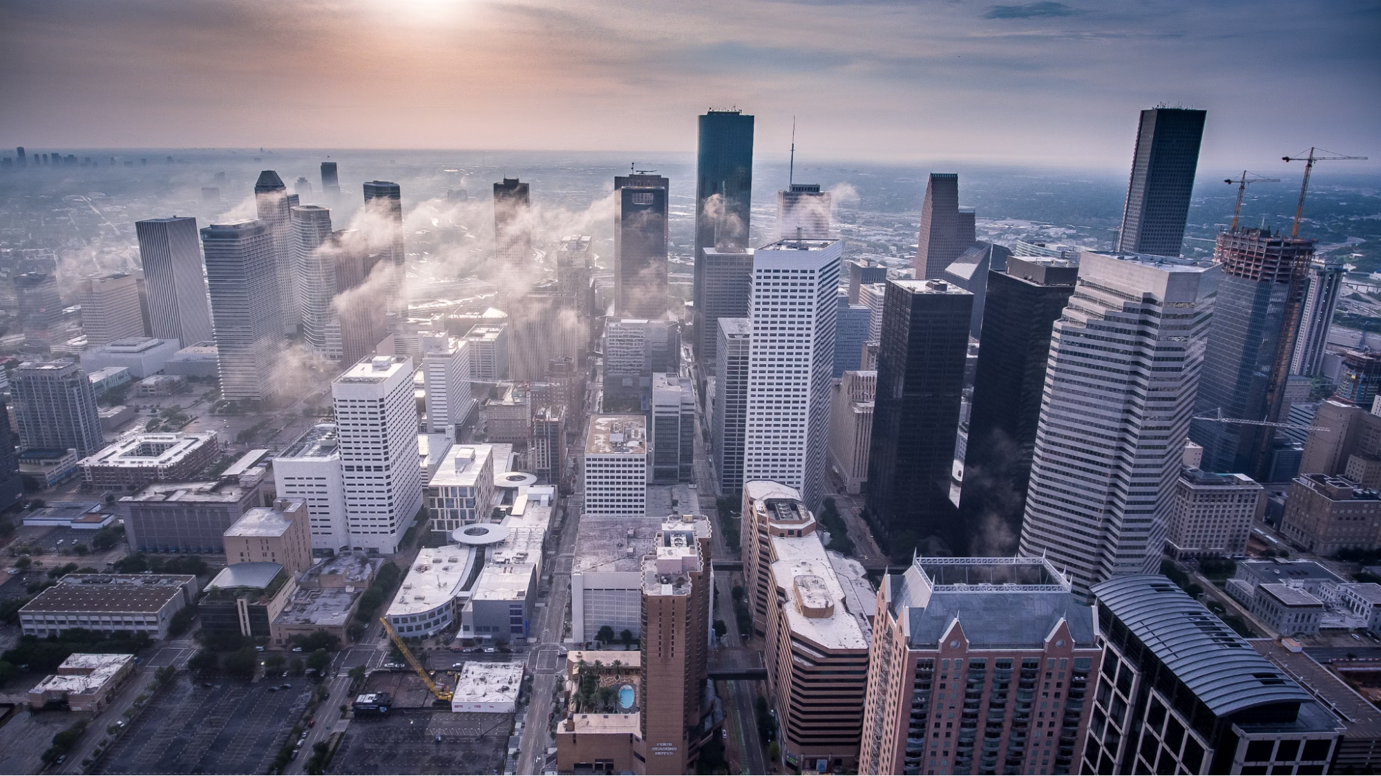photo of a large city scape from the sky with the sun in the background causing glare