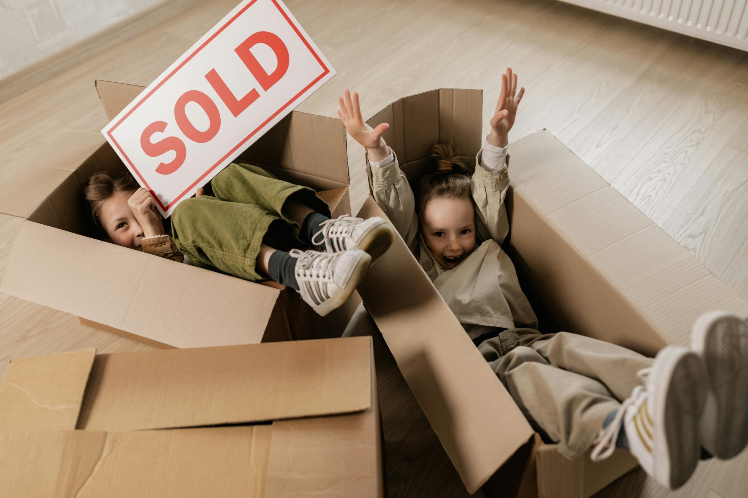 kidsmovingboxes kids playing in boxes while moving with a sold sign in hands